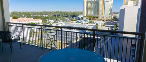 A balcony with a table and chairs, overlooking a parking lot and buildings.