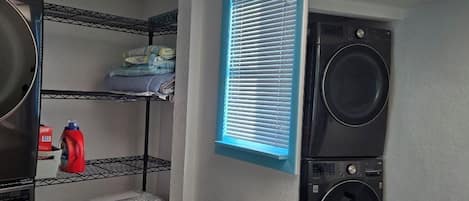 A compact laundry room with a washing machine, dryer, and stacked laundry.