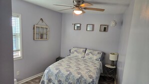 Une chambre à coucher avec un lit, un ventilateur de plafond, une fenêtre et une table de chevet avec une lampe.