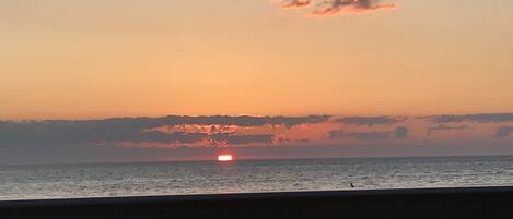 A sunset over the ocean with a person walking on a bridge.