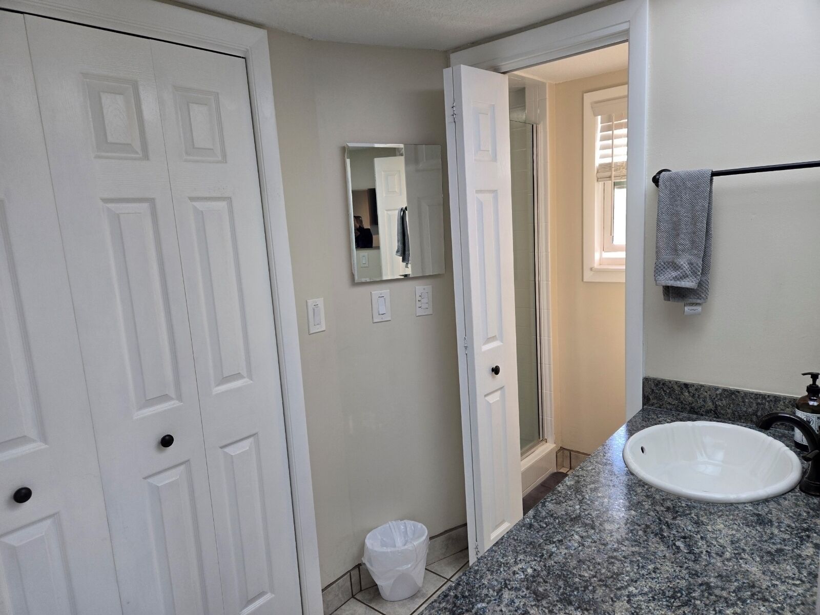 A bathroom with a white sink, a mirror, a towel rack, and a trash bin.