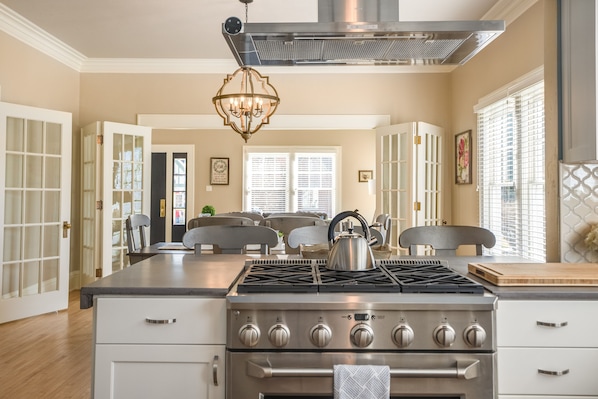 A kitchen with a stainless steel stove, white cabinetry, and a chandelier.