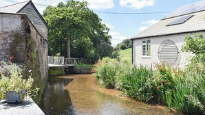 A narrow canal with a wooden bridge, surrounded by lush greenery and a small building with a white facade and a circular window. - 2 bedroom accommodation in Kentisbeare, Cullompton (Kentisbeare, Cullompton)