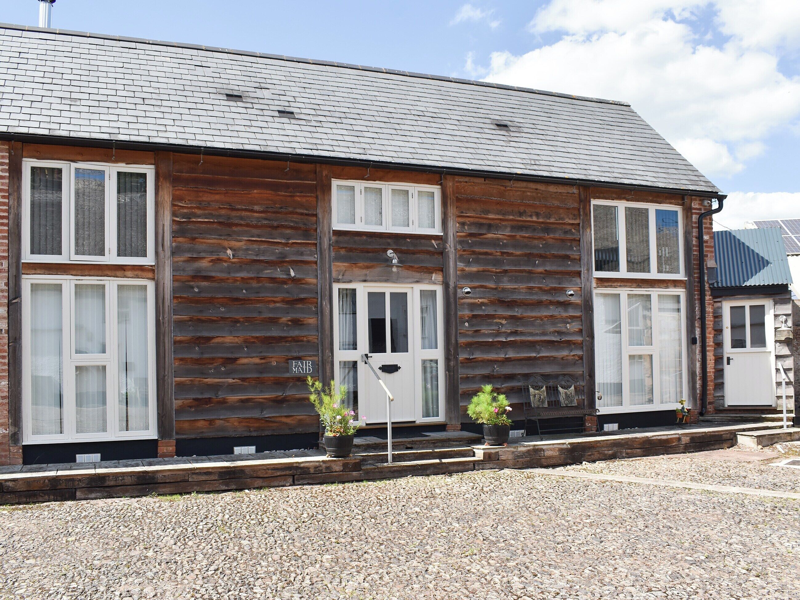 A two-story log cabin with a dark wooden exterior, white-framed windows, and a gravel driveway.