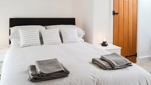 A neatly made bed with striped bedding, a black headboard, and a wooden door in the background. - 2 bedroom accommodation in Kentisbeare, Cullompton (Kentisbeare, Cullompton)