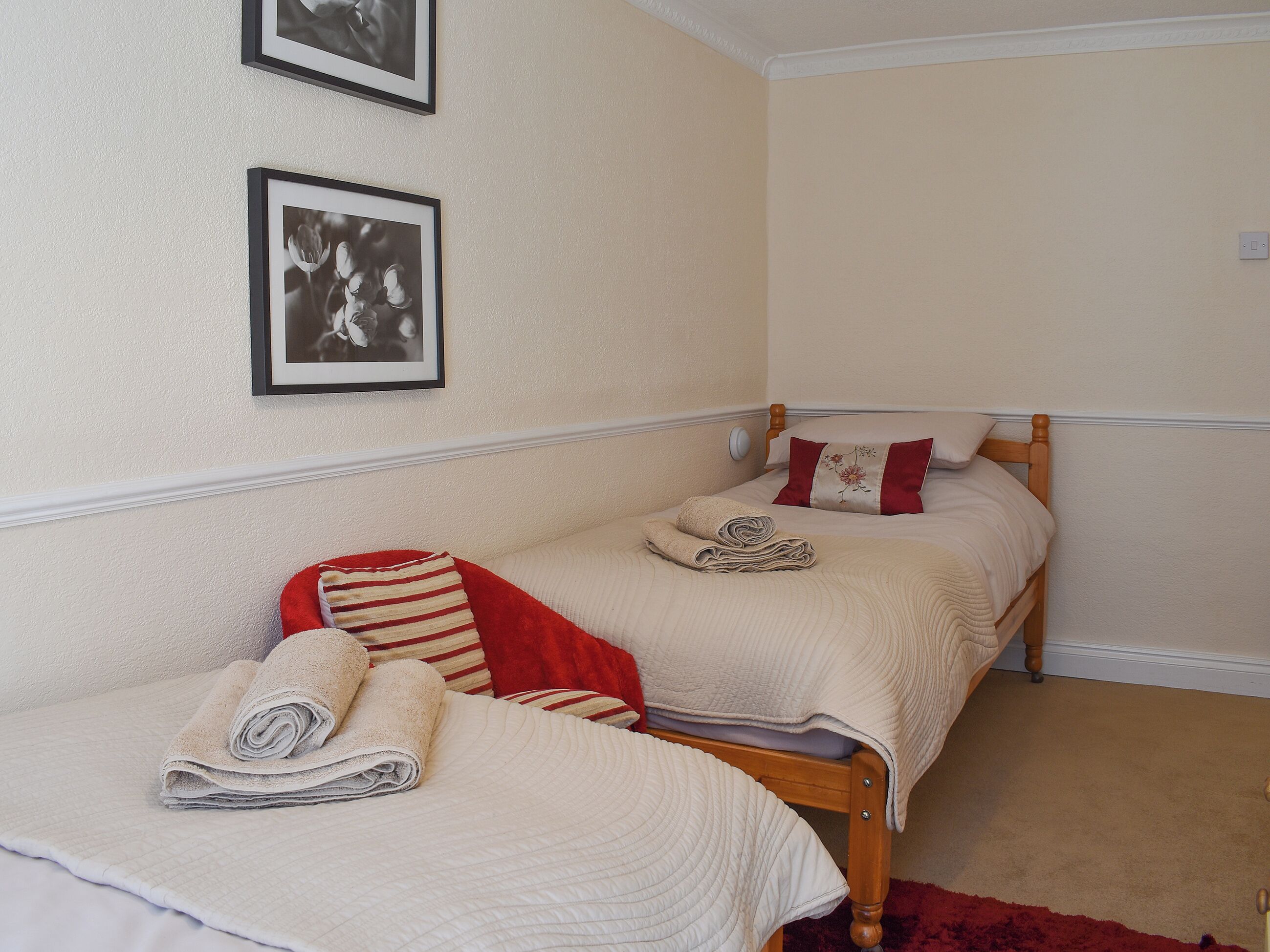A bedroom with two beds, a red and white striped pillow, and two framed pictures on the wall.