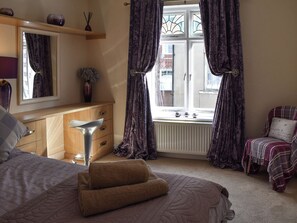 A bedroom with a bed, a dresser, a window with curtains, and a radiator.