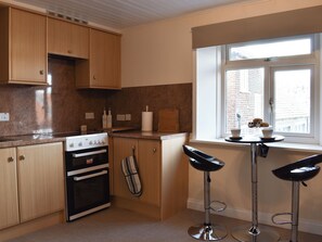 A kitchen with wooden cabinets, a stove, an oven, a window with a view, and two bar stools.
