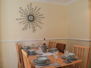 A dining table set with plates, bowls, and glasses, a decorative wall clock, and a wooden chair.