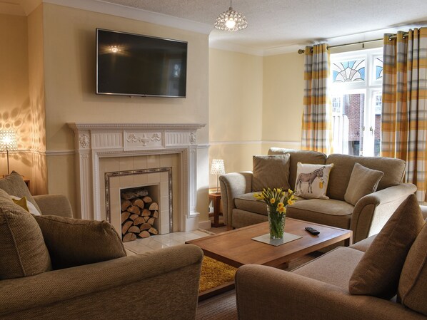 A living room with a fireplace, sofas, a coffee table, and a flat-screen TV mounted on the wall.