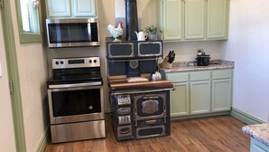 A kitchen with stainless steel appliances, a wood stove, and light green cabinets.