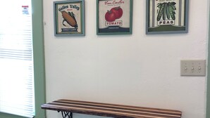 A room with a wooden bench and two black stools against a wall with vintage framed signs.