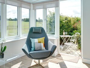 Une chambre moderne avec un fauteuil gris, une petite table et une vue sur un jardin, visible à travers de grandes fenêtres.