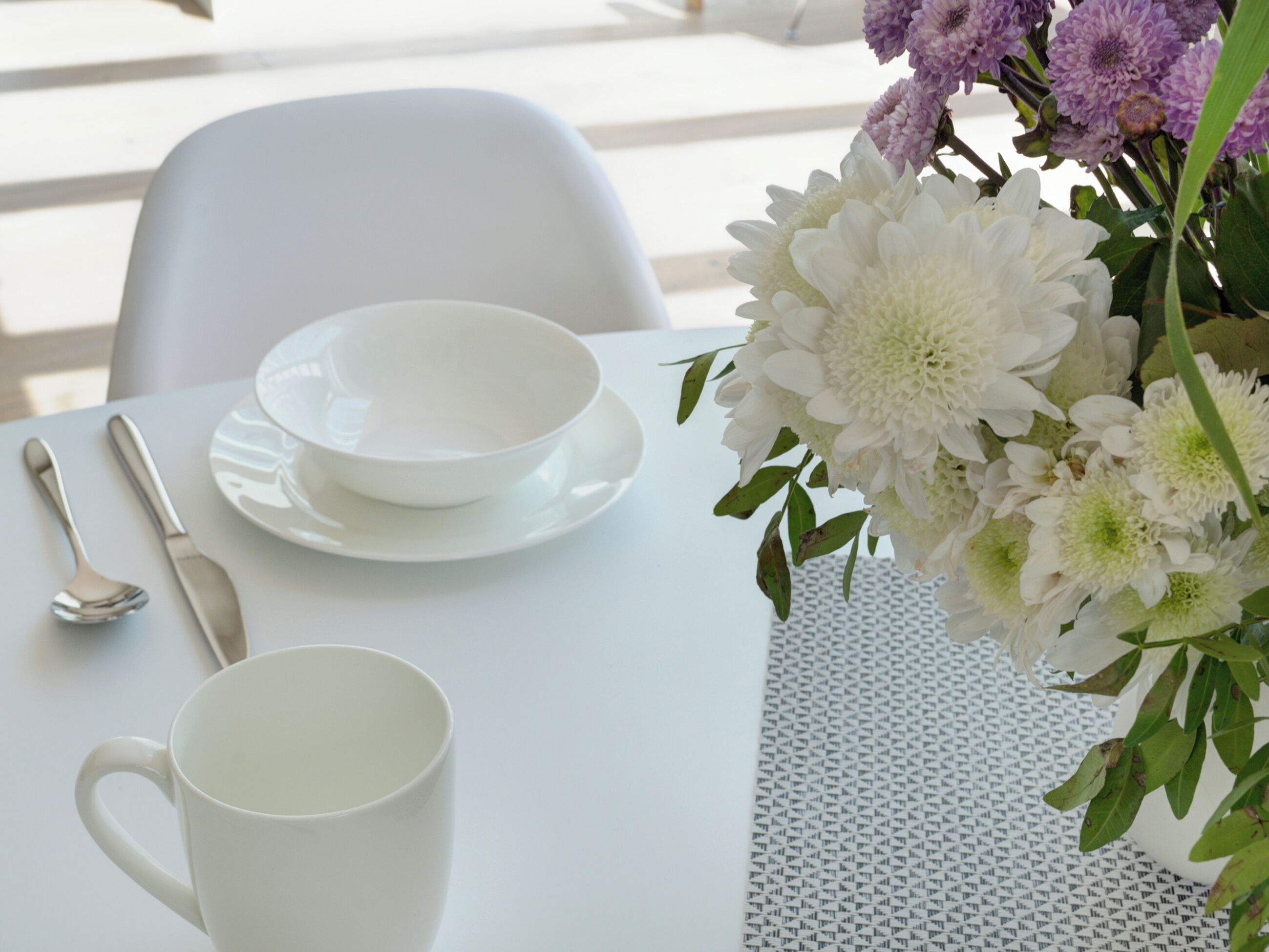 Una mesa dispuesta con vajilla blanca, una taza y un arreglo floral.