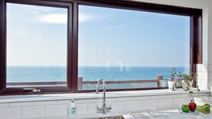 Eine Küche mit großem Fenster zum Meer, einem Spülbecken und einer Arbeitsplatte mit Geschirrständer und Gemüse.