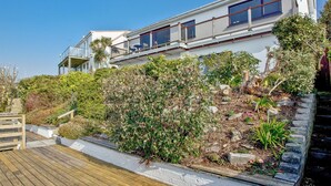 Ein modernes, zweistöckiges Haus mit Balkon, umgeben von üppiger Vegetation und einer Holzterrasse.