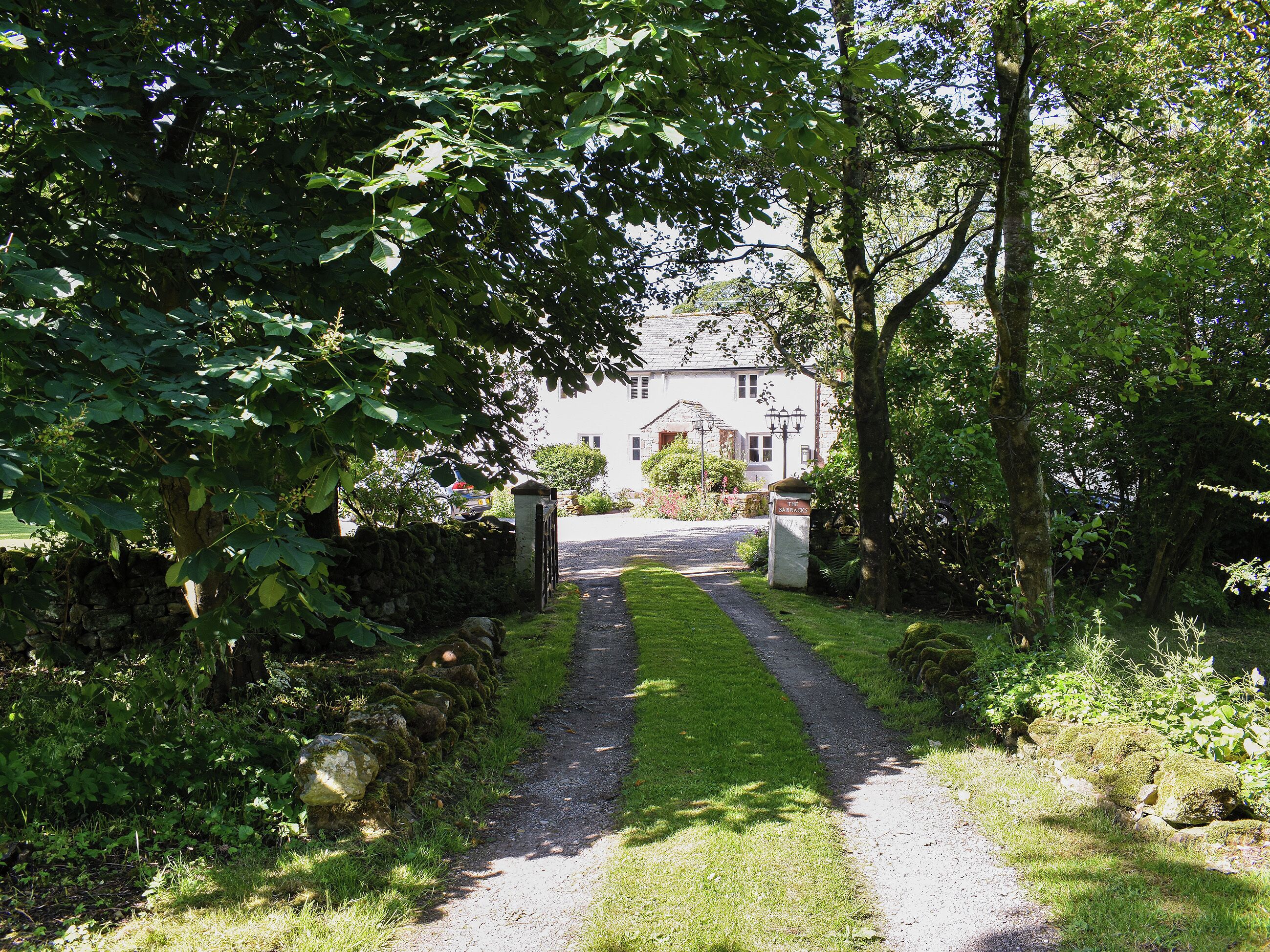 A pathway leading to a building with a stone wall and greenery on either side.