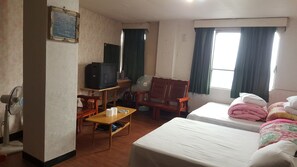 Habitación de hotel con dos camas, un escritorio con televisor, una silla y una ventana con cortinas.