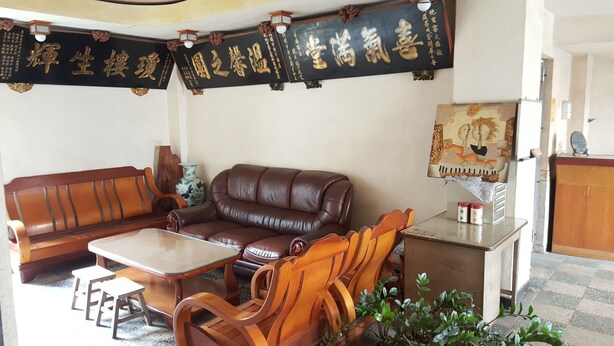 A living room with a brown leather sofa, wooden chairs, a glass-top coffee table, and a small cabinet with jars. - Ta Li Wu Hotel (Dounan)
