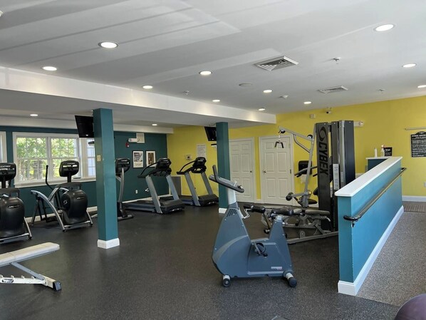 Een fitnessruimte met diverse trainingsapparaten, een receptiebalie en een gele muur.