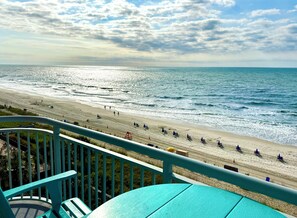 Blick auf einen Strand von einem Balkon mit Geländer, einem Tisch und Stühlen.