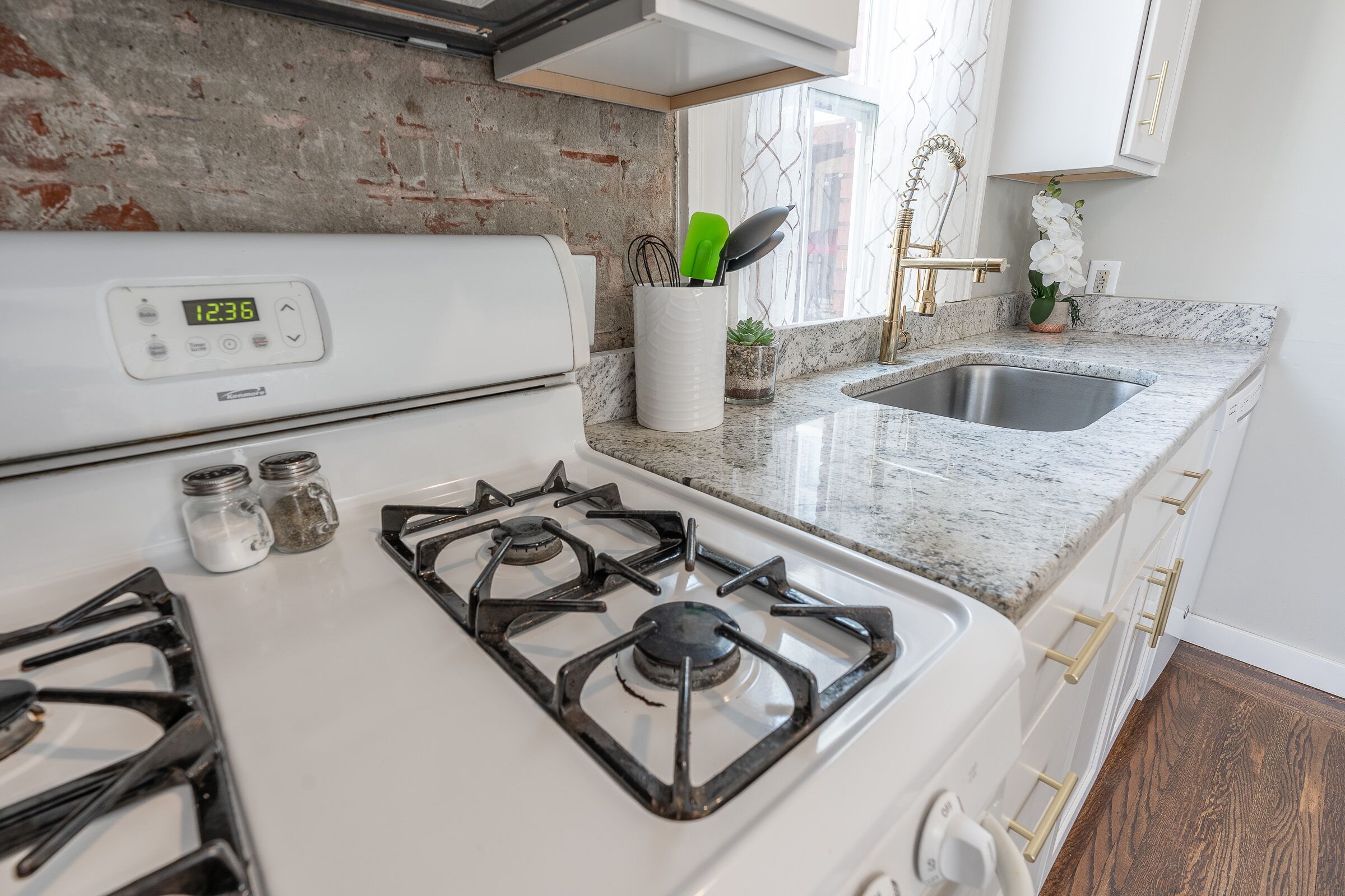 A kitchen with a white stove, stainless steel sink, and granite countertops.