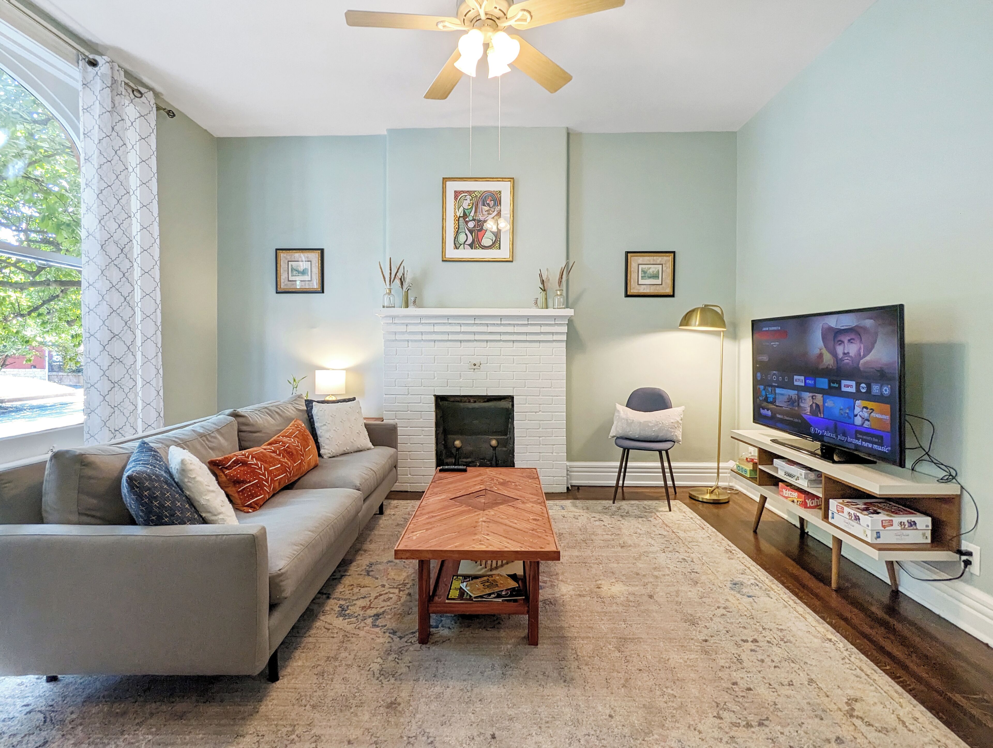A living room with a sofa, coffee table, fireplace, TV, and a ceiling fan.