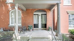 A brick building with a white porch, columns, and a door with a number.