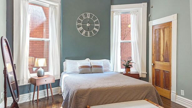 A bedroom with a bed, bedside tables, a clock, a window with curtains, and a door.
