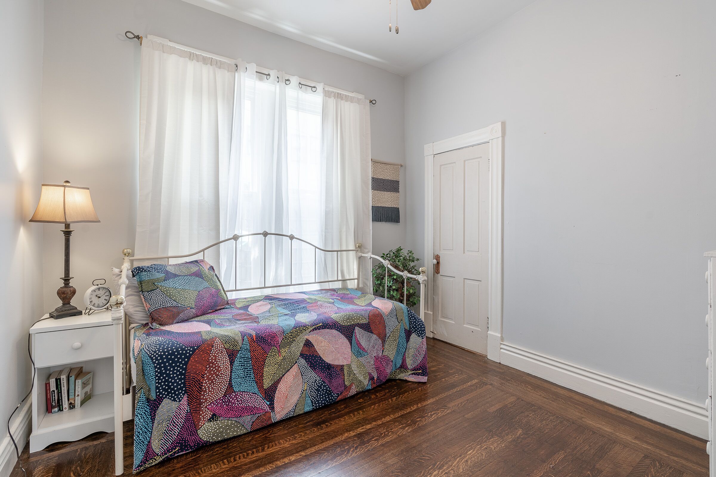 Une chambre à coucher avec un lit, une table de chevet, une lampe, une fenêtre avec des rideaux et une porte.