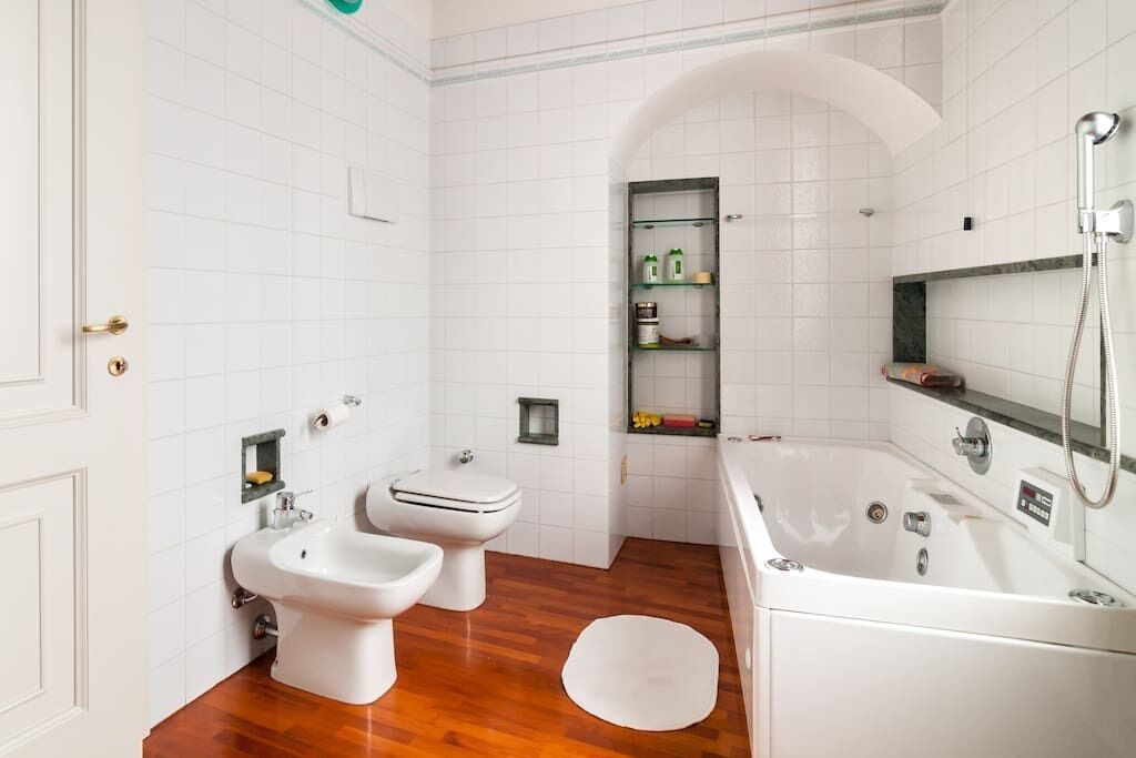 Une salle de bain avec des carreaux blancs, un plancher en bois, un bidet, des toilettes, une baignoire et une douche.
