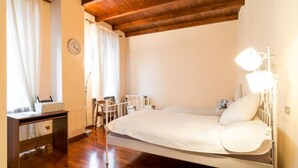 Een slaapkamer met een houten plafond, een bed met een witte hoofdeinde, een nachtkastje, een lamp en een klok aan de muur.