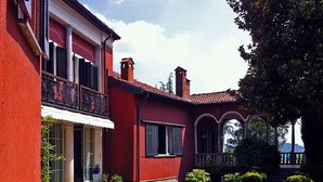 Een rode villa met balkon, overdekte veranda en een tuin.