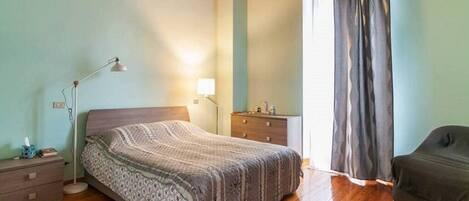 A bedroom with a bed, bedside table, lamp, dresser, and a window with curtains.