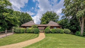 A two-story house with a symmetrical roof and a gravel driveway leading to a wooden gate. - Castlemans Stables West (Sedlescombe, near Battle)