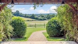 A wooden pergola with hanging lamps and a gravel path leading to a fenced field. - Castlemans Stables West (Sedlescombe, near Battle)