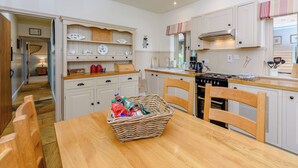 A kitchen with white cabinetry, a wooden table, and a basket of items. - Castlemans Stables West (Sedlescombe, near Battle)