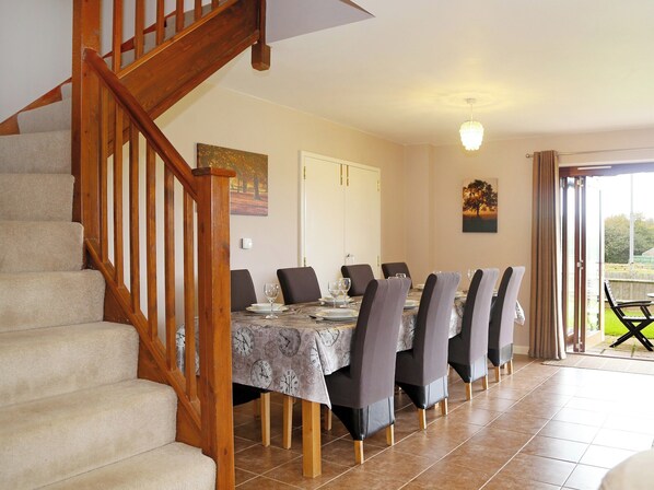 Un comedor con una escalera de madera, una mesa para seis personas y vistas al exterior a través de una puerta corrediza de vidrio.