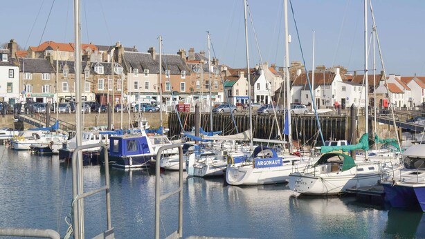 A marina with multiple boats docked, a clear sky, and buildings in the background. - The Lodge at Lochnagar (Peat Inn, near St Andrews)