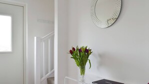 A hallway with a white door, a staircase, a glass vase with flowers, and a book titled "Visitors" on a white table. - The Lodge at Lochnagar (Peat Inn, near St Andrews)