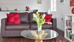 A modern living room with a brown leather sofa, a glass coffee table, and a bookshelf filled with books. - The Lodge at Lochnagar (Peat Inn, near St Andrews)