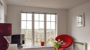 A modern living room with a large window, a red chair, a glass coffee table, and a flat-screen TV. - The Lodge at Lochnagar (Peat Inn, near St Andrews)