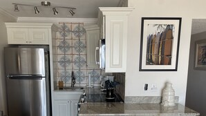 A modern kitchen with white cabinetry, a stainless steel refrigerator, a marble countertop, and a coffee maker. - Enjoy an oceanfront getaway with beautiful beach steps from your door.   (North Topsail Beach)