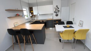 A modern kitchen with a central island, bar stools, a dining table with yellow chairs, and a refrigerator. - SORRISO 2 Two-Bedroom Apartment (Rovinj)