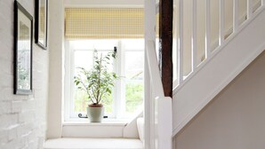 A staircase with a potted plant on the landing, white walls, and a window with a checkered blind.