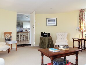 Ein Wohnzimmer mit Essbereich, einem weißen Sessel, einem Holztisch mit Büchern und einem gerahmten Bild an der Wand.