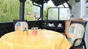 A covered outdoor seating area with a yellow tablecloth, chairs with colorful patterns, and a view of greenery and buildings in the background. - Beautiful apartment for 6 people with WIFI, TV, terrace and panoramic view (Hippach)