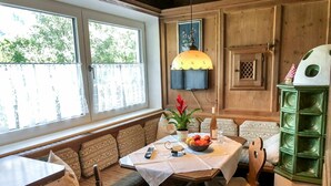 A cozy kitchen with a dining table, bench seating, a green cabinet, and a window with curtains. - Beautiful apartment for 6 people with WIFI, TV, terrace and panoramic view (Hippach)