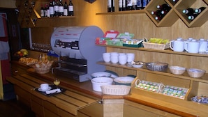 Een buffetopstelling met diverse soorten eten, een koffieapparaat en wijnflessen op planken.