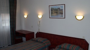 Een hotelkamer met twee eenpersoonsbedden, een bureau, een stoel, een telefoon en een schilderij aan de muur.